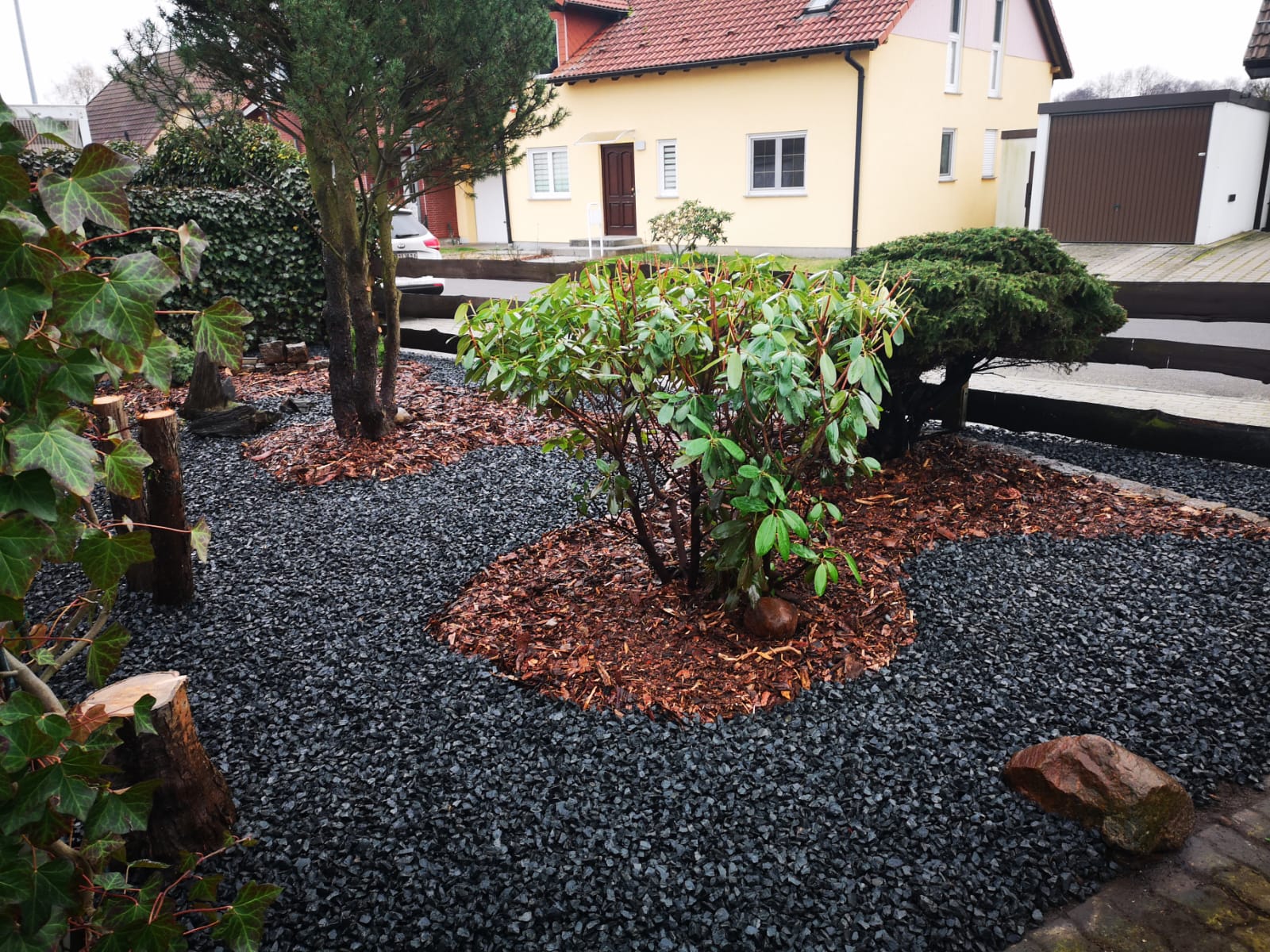 Pflegeleichter Vorgarten mit Kies, Rindenmulch und Rhododendron vor Einfamilienhaus